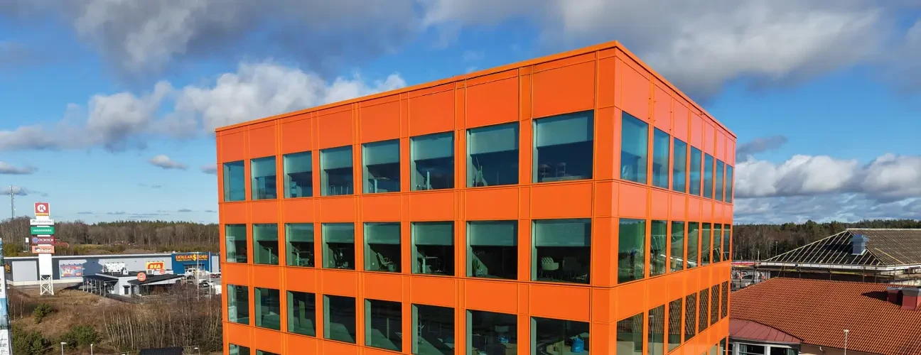 Färgglad orange byggnad med stora fönster och blå himmel. Kontakt.