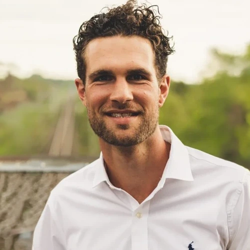 En man med lockig frisyr ler framför grönskande landskap.