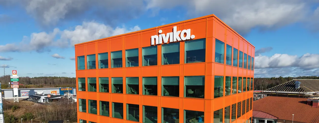 Ljusorange modern kontorsbyggnad med stora fönster och nivika.logotypen i det övre hörnet.